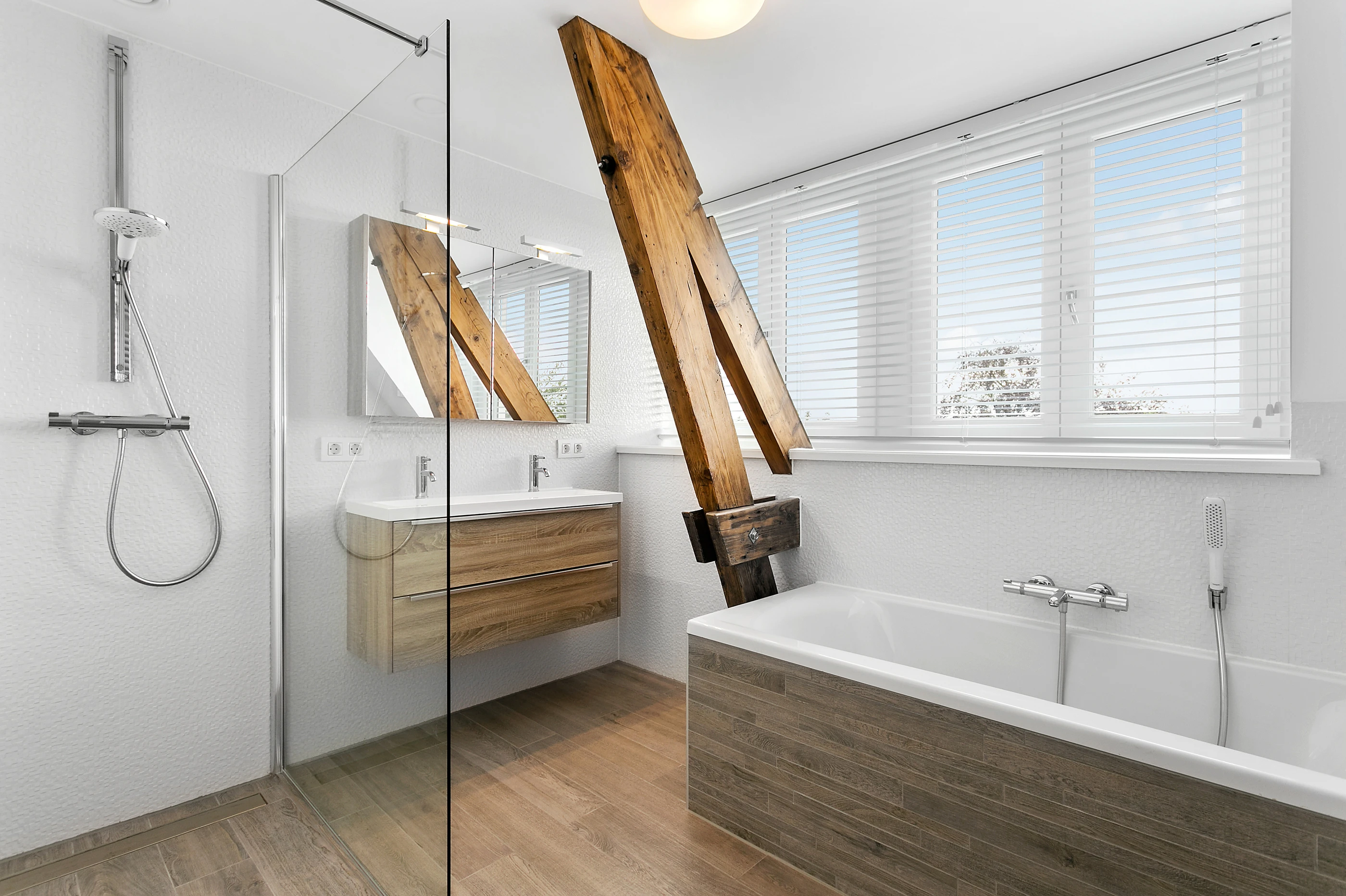 Badkamer met inloopdouche en ligbad onder een oude houten spant