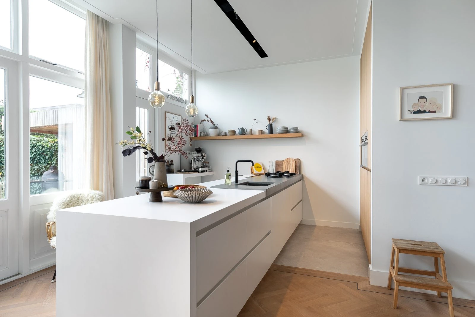 Witte keuken met een lang eiland en glazen hanglampen bij de tuindeuren