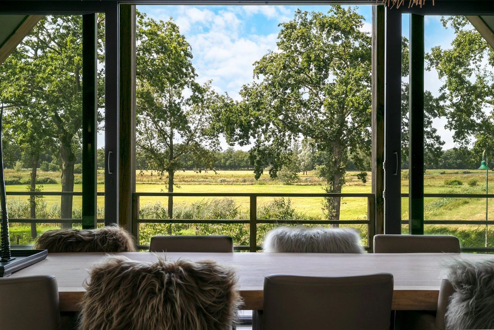 Eettafel met schapenvachten, uitkijkend over een weiland met eiken