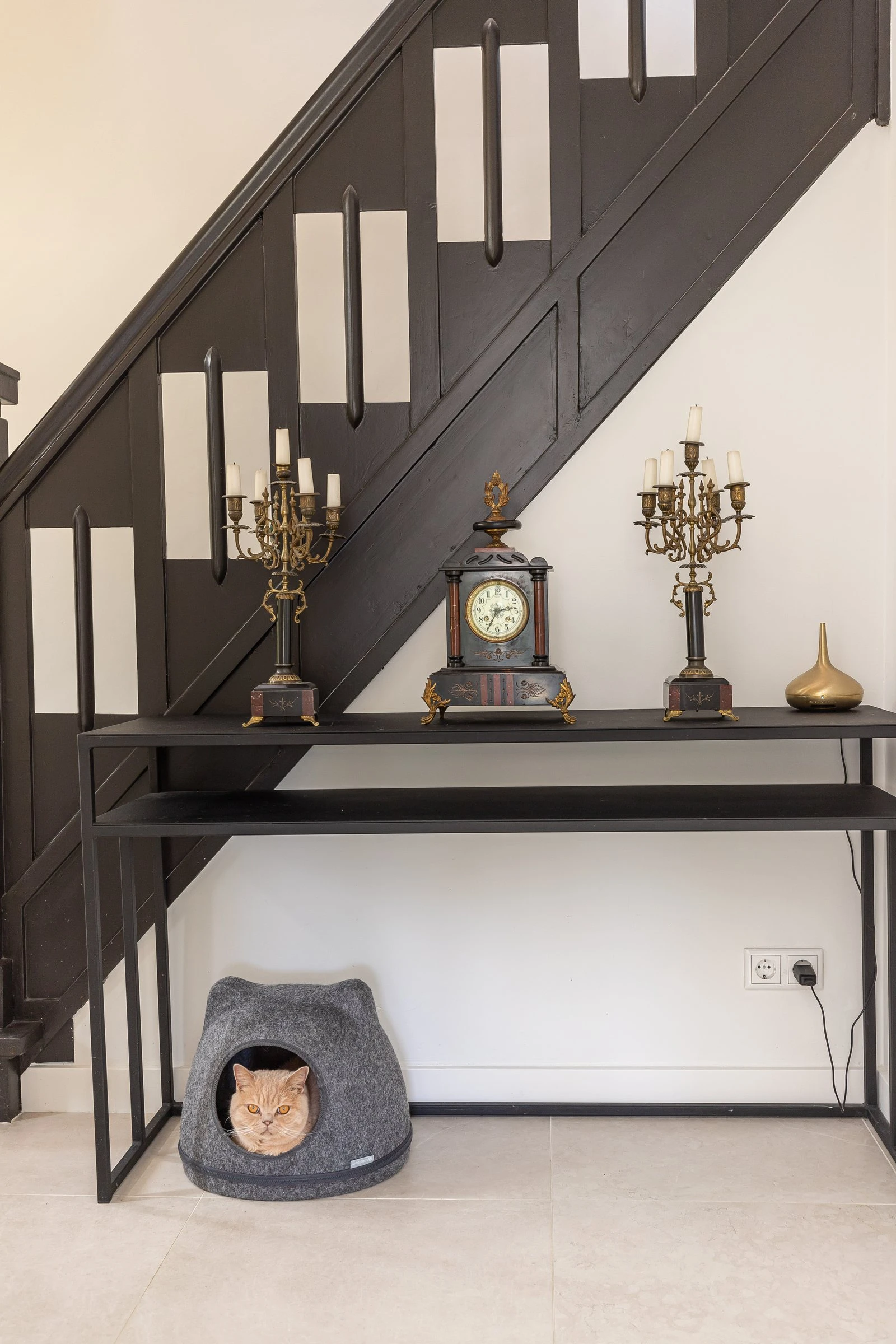 Zwart wandmeubel onder de trap met twee klokken en een kattenmand