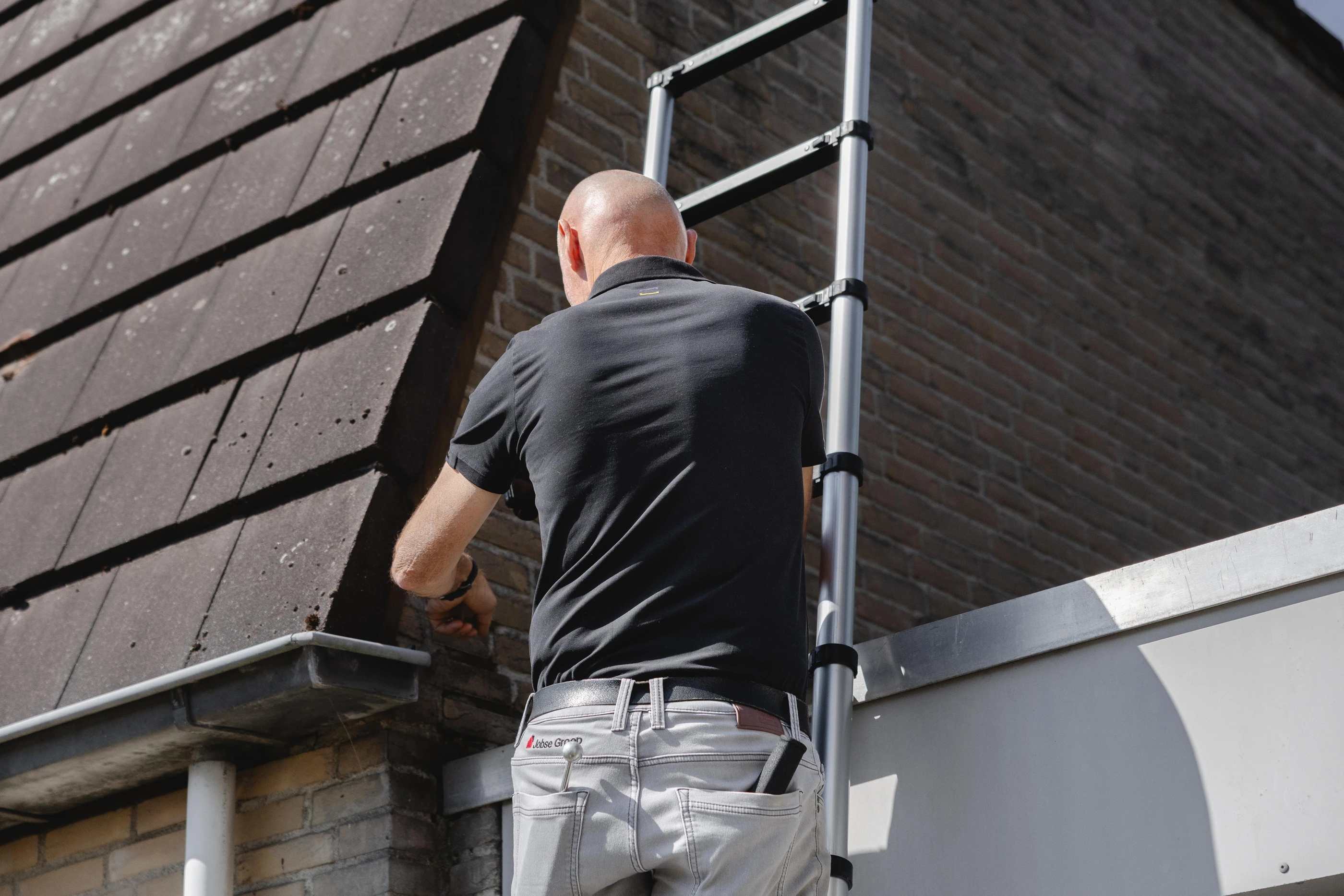 Inspecteur op een ladder bij de dakgoot van een woning